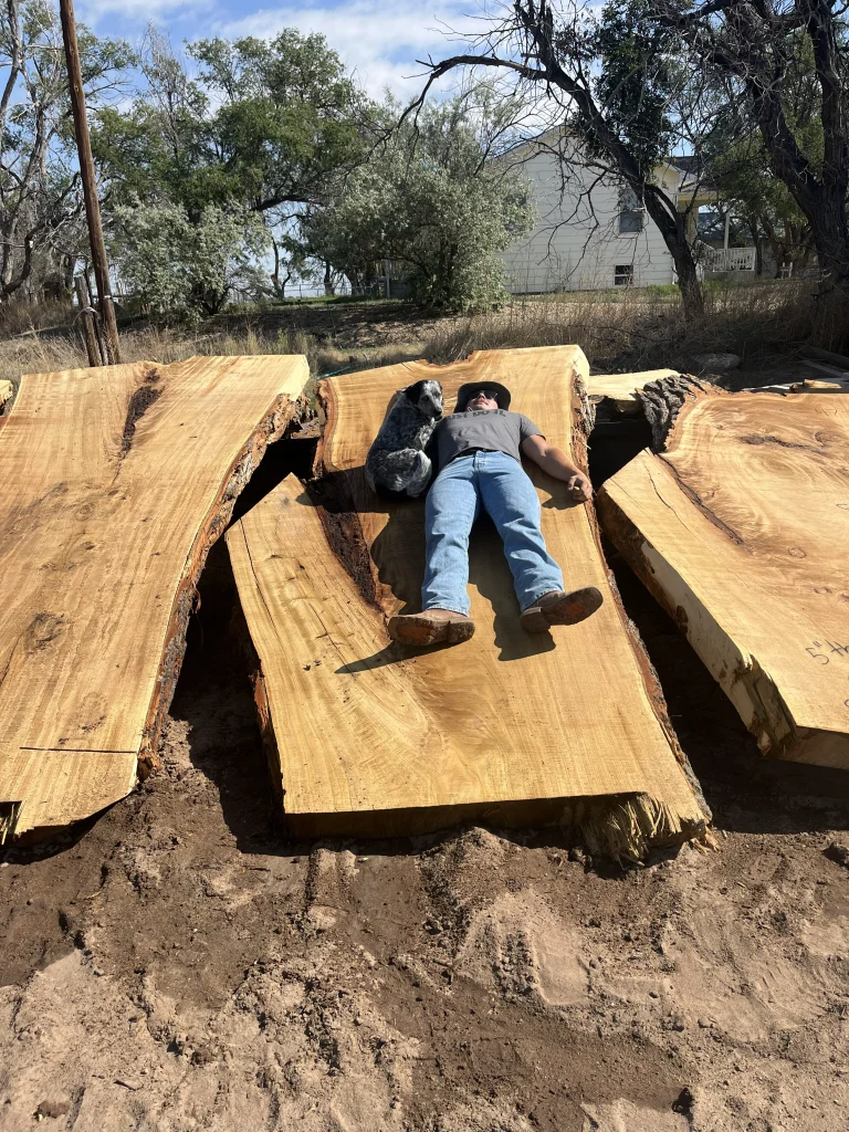 Three large slabs of lumber laid side by side with a man and a dog laying on the middle slab 
